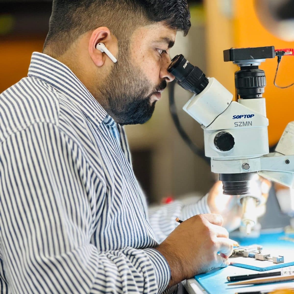 Shiv Sharma inspecting a logic board under a stereo microscope at the Shiv i Care workshop in Ludhiana